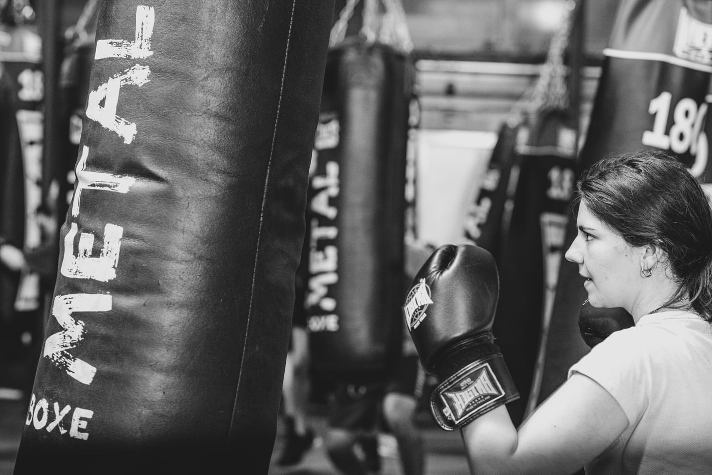 Une boxeuse en garde face au sac de frappe, en noir et blanc